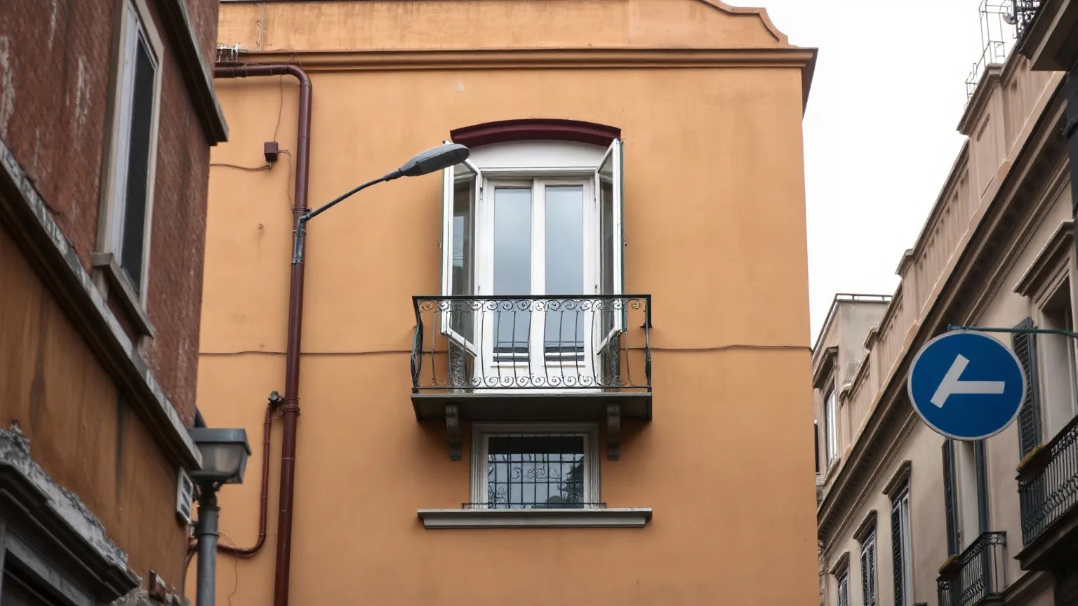Un balcone con la ringhiera in ferro su una facciata color ocra, visto dalla strada